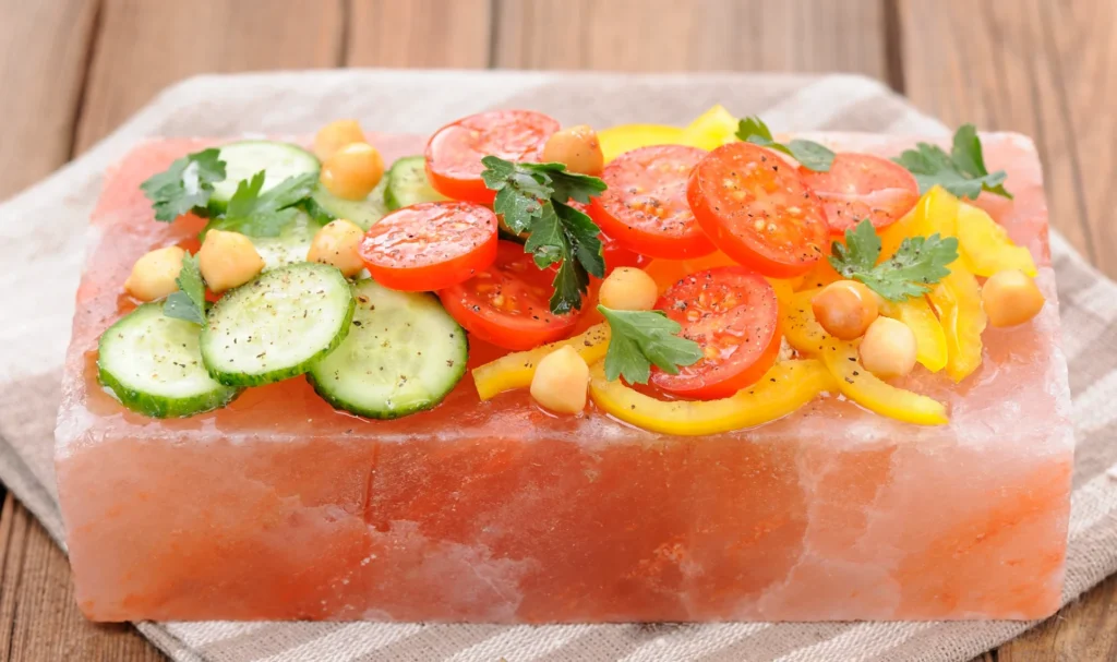 A fresh salad of sliced tomatoes, cucumbers, chickpeas, and yellow peppers served directly on a cold pink Himalayan salt block.